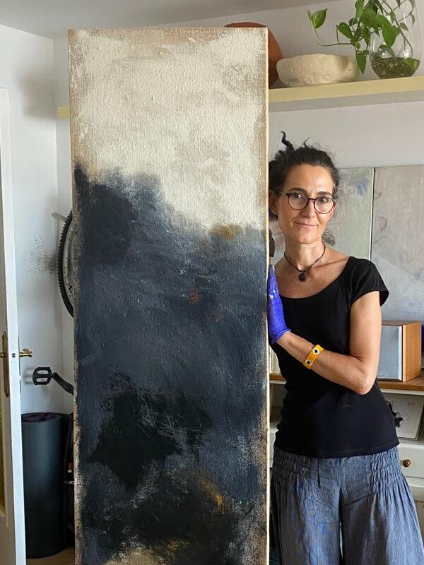 Fotografía de la artista Cruz Calderón Lamas sosteniendo una de sus obras en formato vertical.